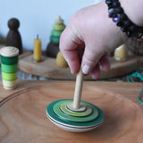 Mader wooden my first spinning top toy with starter in green placed on a large cherry wood spinning plate in the Babipur playroom.