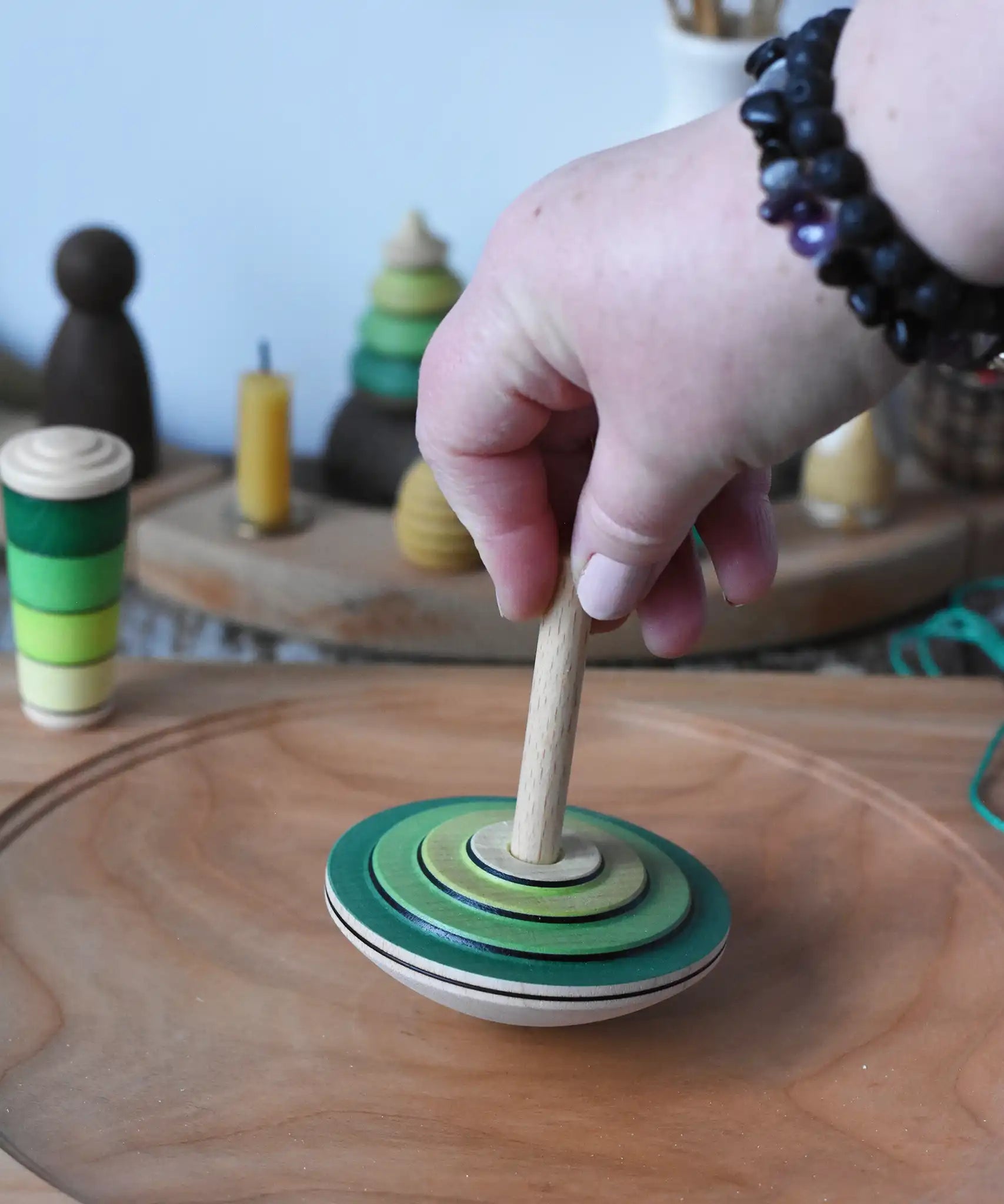 Mader wooden my first spinning top toy with starter in green placed on a large cherry wood spinning plate in the Babipur playroom.