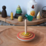 Close up of the Mader wooden my first spinning top toy with starter in orange spinning in motion on a spinning plate in the Babipur playroom.