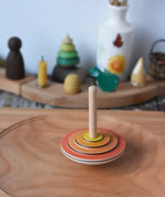 Close up of the Mader wooden my first spinning top toy with starter in orange spinning in motion on a spinning plate in the Babipur playroom.