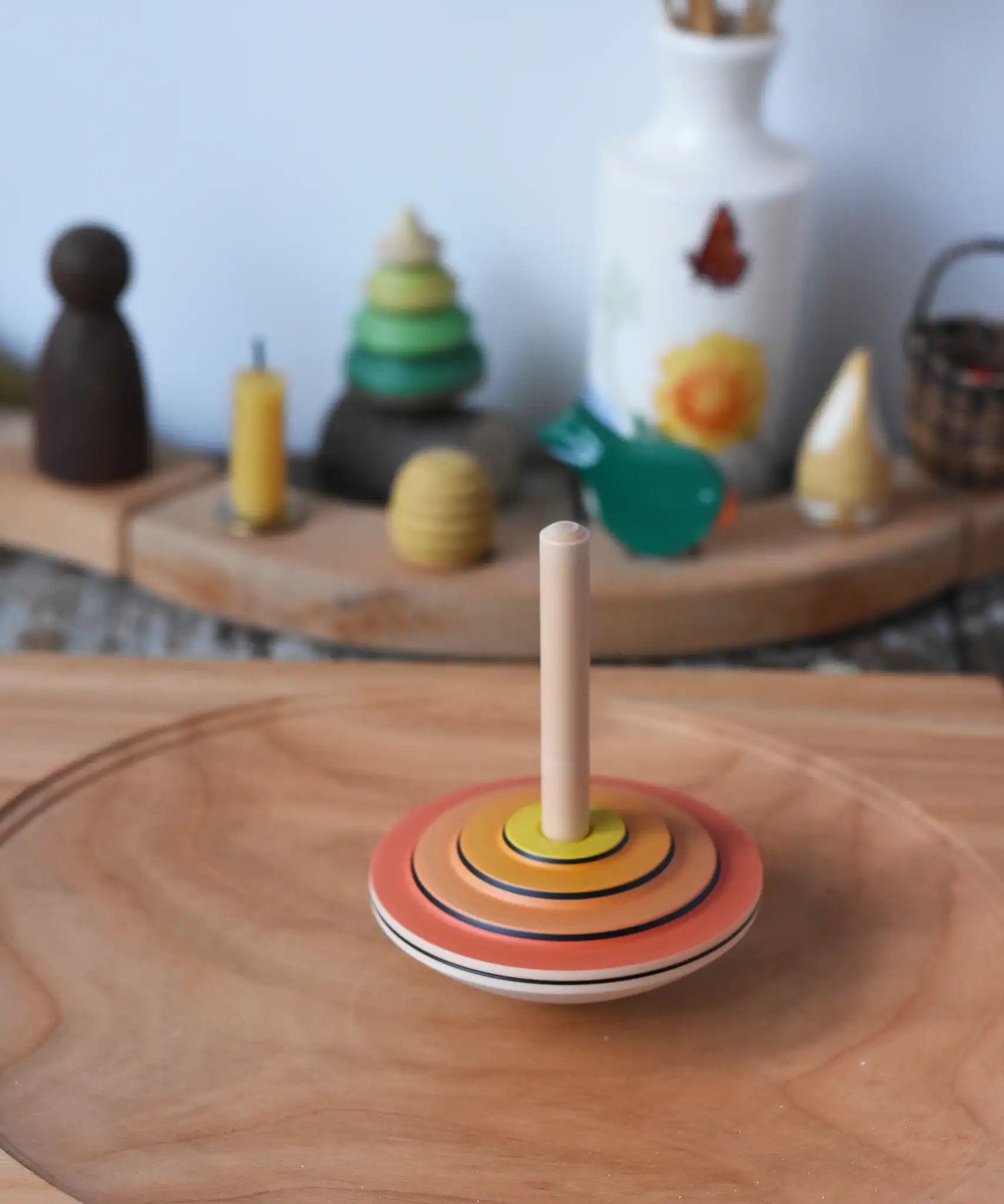Close up of the Mader wooden my first spinning top toy with starter in orange spinning in motion on a spinning plate in the Babipur playroom.