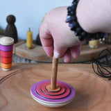 Close up of an adult's hand placing the Mader my first spinning top toy with starter in pink on a large cherry wood spinning plate in the Babipur playroom. 