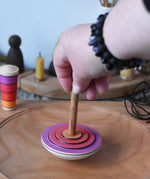 Close up of an adult's hand placing the Mader my first spinning top toy with starter in pink on a large cherry wood spinning plate in the Babipur playroom. 