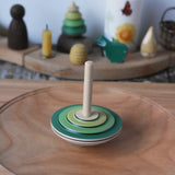 Mader wooden my first spinning top toy with starter in green spinning in motion on a large cherry wood spinning plate in the Babipur playroom.