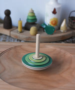 Mader wooden my first spinning top toy with starter in green spinning in motion on a large cherry wood spinning plate in the Babipur playroom.