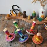 A collection of 5 different colours of Mader my first spinning top toys with starter placed on a wooden surface in the Babipur playroom. 