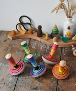 A collection of 5 different colours of Mader my first spinning top toys with starter placed on a wooden surface in the Babipur playroom. 