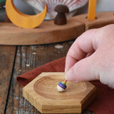 Mader hexagon 8cm spinning top plates in oak with a tiny rainbow spinning top being placed on it.