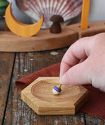 Mader hexagon 8cm spinning top plates in oak with a tiny rainbow spinning top being placed on it.