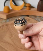 Top of Mader orient turn-over spinning top, held in an adult's hand.