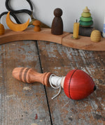 Mader red pull-string spinning top placed on a wooden surface in the Babipur playroom.