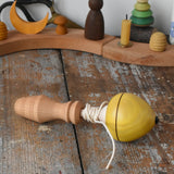 Mader yellow pull-string spinning top spinning placed on a wooden surface in the Babipur playroom.