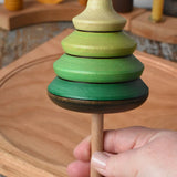 Mader pull-string tree spinning top in an adult's hand with a cherry wood spinning plate in the background in the Babipur playroom.