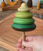 Mader pull-string tree spinning top in an adult's hand with a cherry wood spinning plate in the background in the Babipur playroom.
