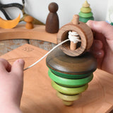 Mader pull-string tree spinning top placed on a cherry wood spinning plate in the Babipur playroom. A child'd hand can be seen holding the wooden handle and pulling the string.