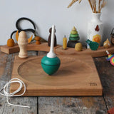 Mader green pull-string spinning top spinning on a large oak spinning plate in the Babipur playroom.