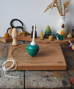 Mader green pull-string spinning top spinning on a large oak spinning plate in the Babipur playroom.