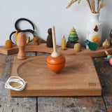 Mader orange pull-string spinning top spinning on a large oak spinning plate in the Babipur playroom.