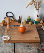 Mader orange pull-string spinning top spinning on a large oak spinning plate in the Babipur playroom.
