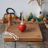 Mader red pull-string spinning top spinning on a large oak spinning plate in the Babipur playroom.