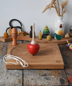 Mader red pull-string spinning top spinning on a large oak spinning plate in the Babipur playroom.
