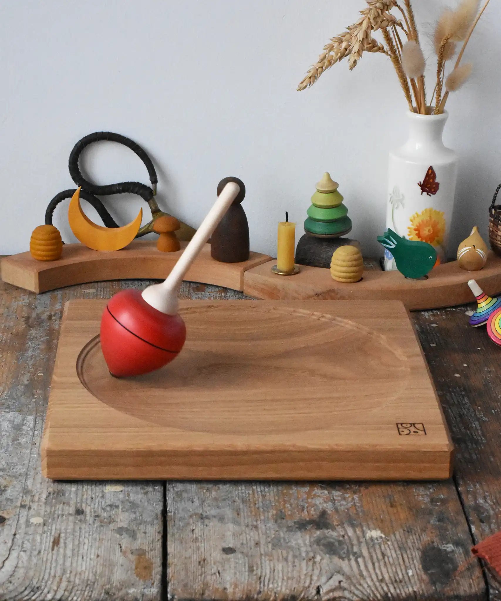 Mader red pull-string spinning top spinning on a large oak spinning plate in the Babipur playroom.