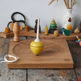 Mader yellow pull-string spinning top spinning on a large oak spinning plate in the Babipur playroom.