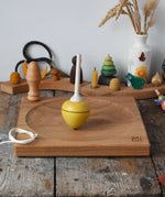 Mader yellow pull-string spinning top spinning on a large oak spinning plate in the Babipur playroom.