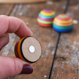 Mader striped wooden magnet  in an adult hand showing the magnet piece on the back. 