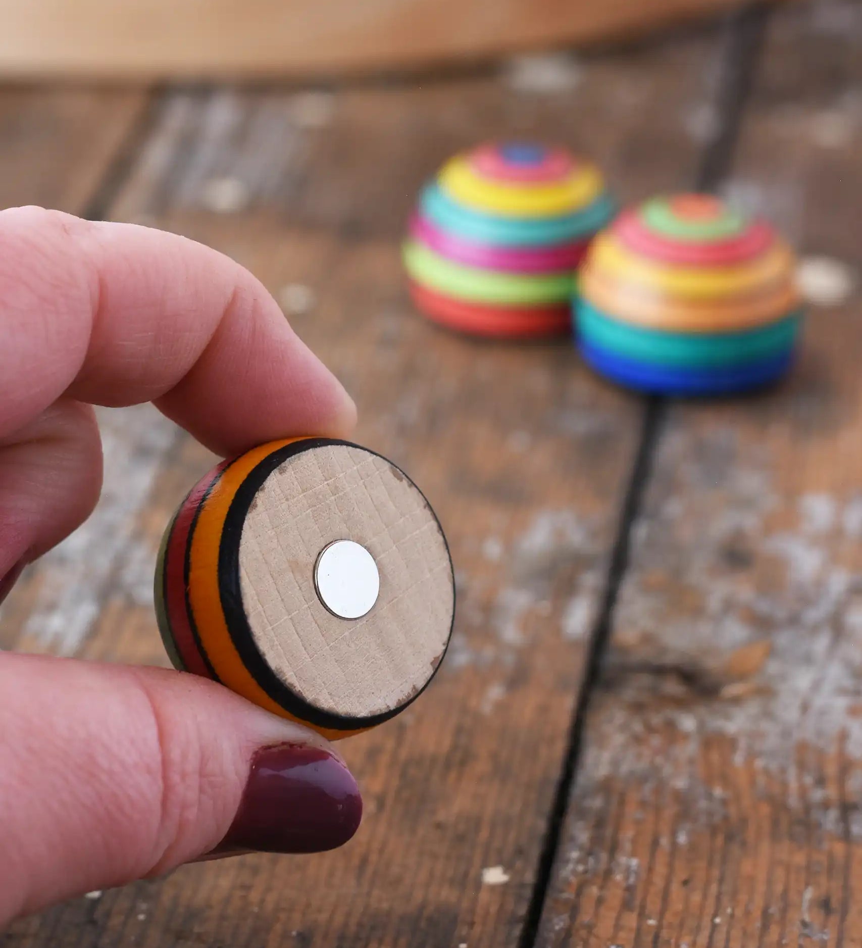 Mader striped wooden magnet  in an adult hand showing the magnet piece on the back. 