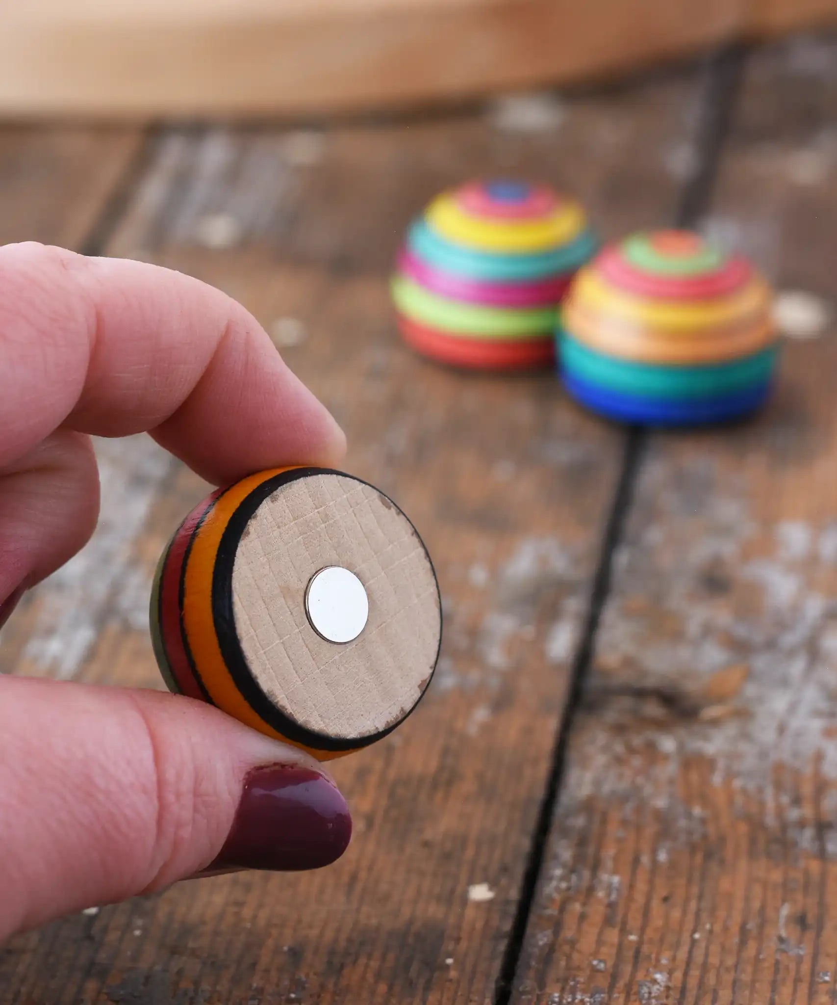 Mader striped wooden magnet  in an adult hand showing the magnet piece on the back. 