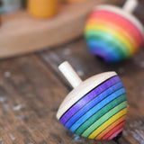 Mader Kreiselmanufaktur rainbow egg spinning top placed on a wooden surface in the Babipur playroom. Another spinner can be seen in the background. 