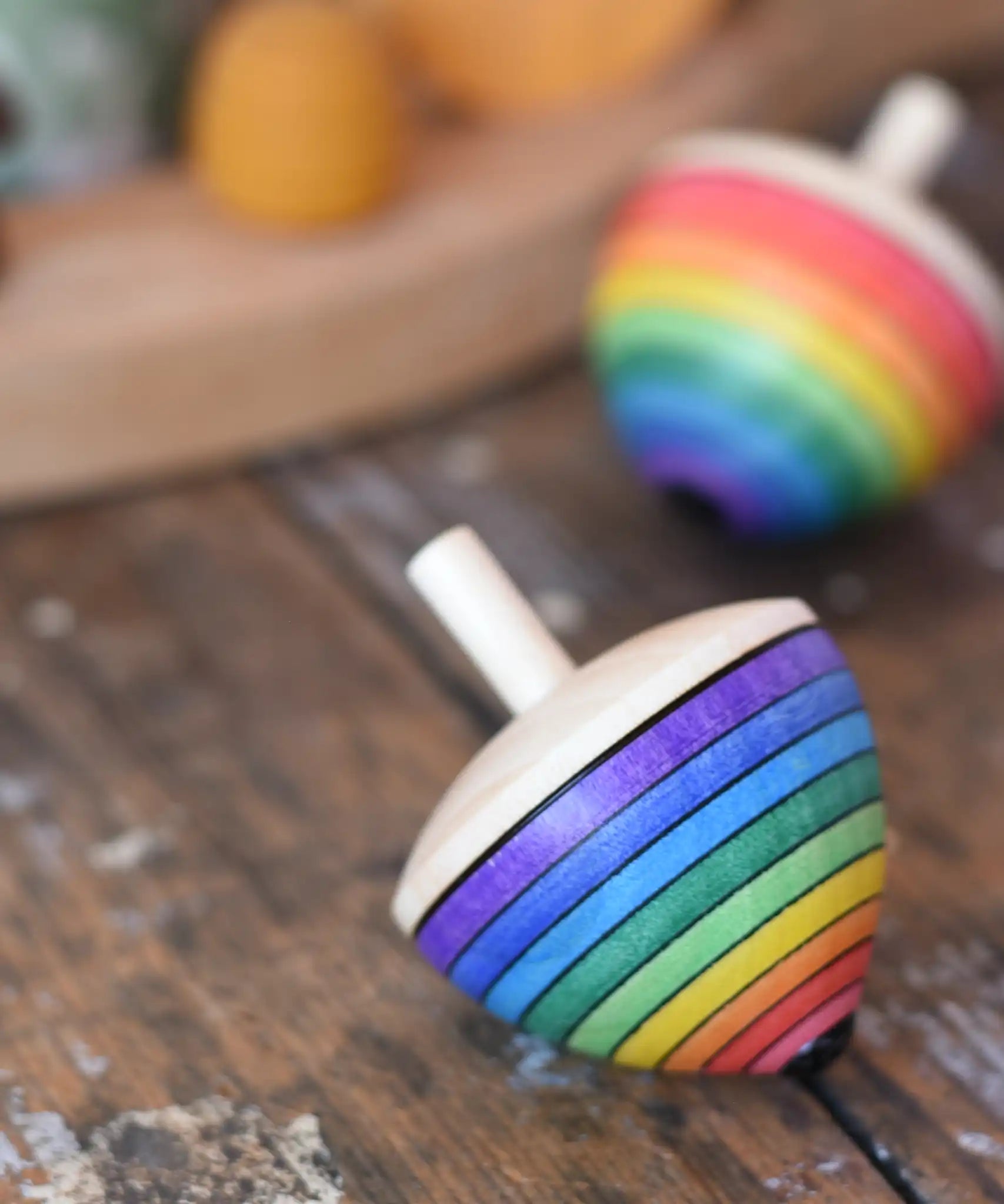 Mader Kreiselmanufaktur rainbow egg spinning top placed on a wooden surface in the Babipur playroom. Another spinner can be seen in the background. 
