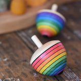 Mader Kreiselmanufaktur rainbow egg spinning top placed on a wooden surface in the Babipur playroom. Another spinner can be seen in the background