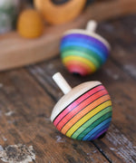 Mader Kreiselmanufaktur rainbow egg spinning top placed on a wooden surface in the Babipur playroom. Another spinner can be seen in the background