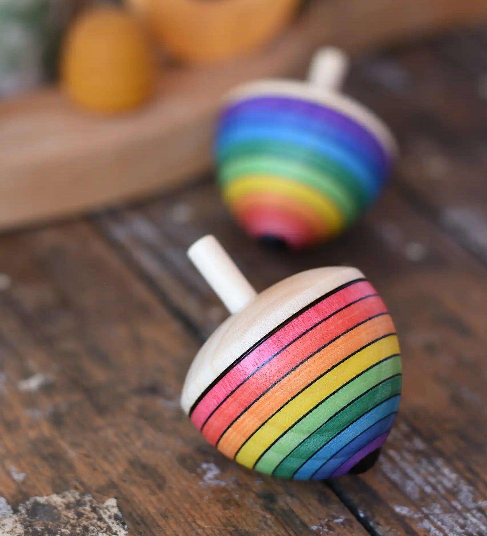 Mader Kreiselmanufaktur rainbow egg spinning top placed on a wooden surface in the Babipur playroom. Another spinner can be seen in the background