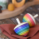 Mader Kreiselmanufaktur rainbow egg spinning top placed on a cloth on a wooden surface in the Babipur playroom. Another spinner can be seen in the background. 