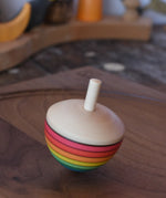 Mader Kreiselmanufaktur rainbow egg spinning top spinning in motion on a walnut wood plate in the Babipur playroom.