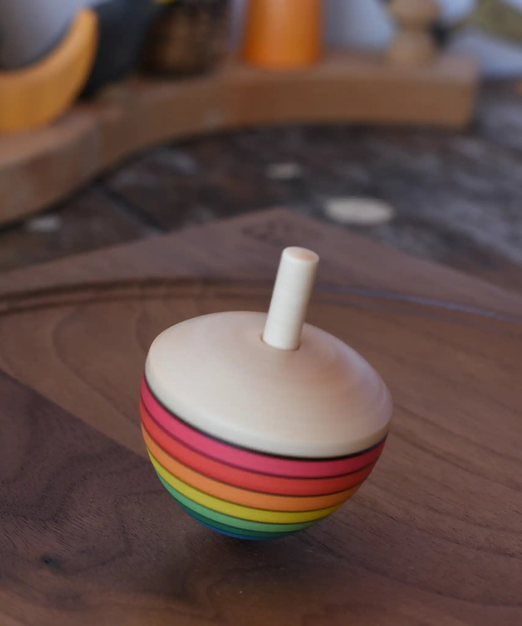 Mader Kreiselmanufaktur rainbow egg spinning top spinning in motion on a walnut wood plate in the Babipur playroom.