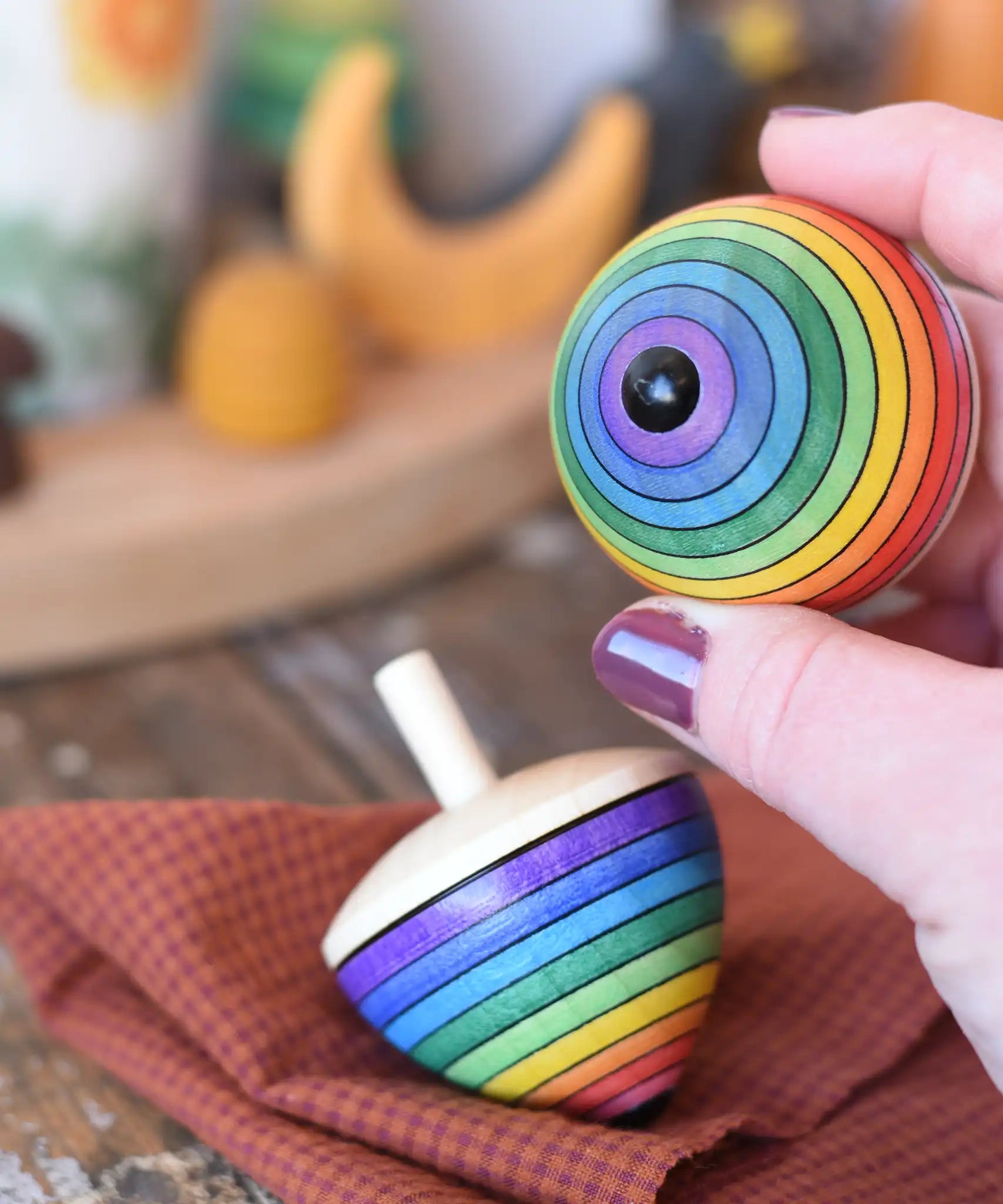 Metal tip on the bottom of a Mader Kreiselmanufaktur rainbow egg spinning top in an adult's hand.