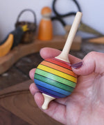 Mader Kreiselmanufaktur rainbow lolly spinning top in an adult's hand in the Babipur playroom.