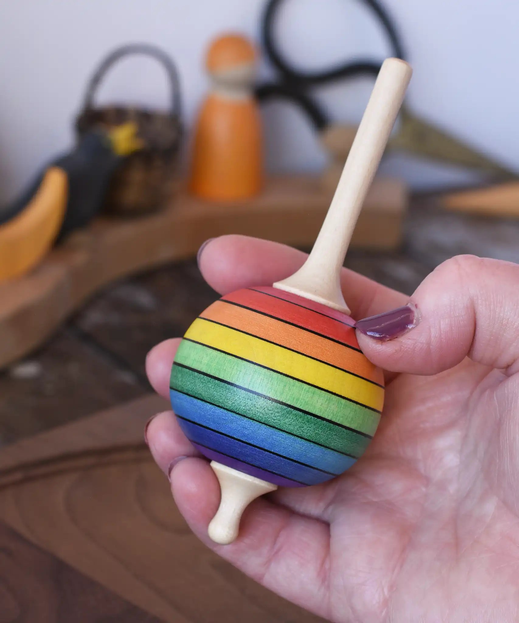 Mader Kreiselmanufaktur rainbow lolly spinning top in an adult's hand in the Babipur playroom.