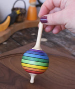 Mader Kreiselmanufaktur rainbow lolly spinning top being placed on a walnut wood spinning plate in the Babipur playroom.