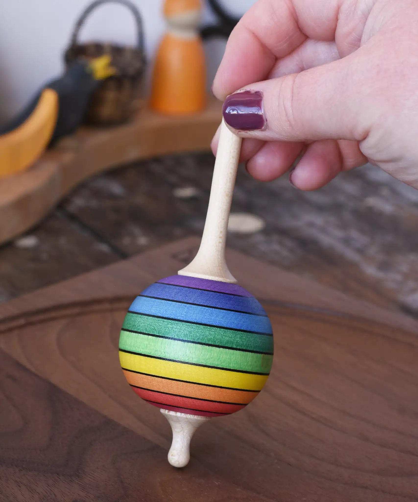 Mader Kreiselmanufaktur rainbow lolly spinning top being placed on a walnut wood spinning plate in the Babipur playroom.