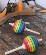 Two Mader Kreiselmanufaktur rainbow lolly spinning tops placed on a wooden surface in the Babipur playroom.