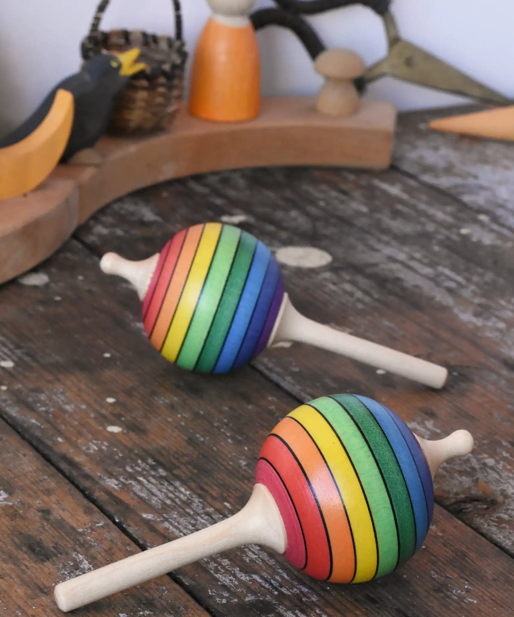 Two Mader Kreiselmanufaktur rainbow lolly spinning tops placed on a wooden surface in the Babipur playroom.