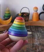 Mader wooden rainbow roly-poly wobbly pear toy in an adult's hand in the Babipur playroom.