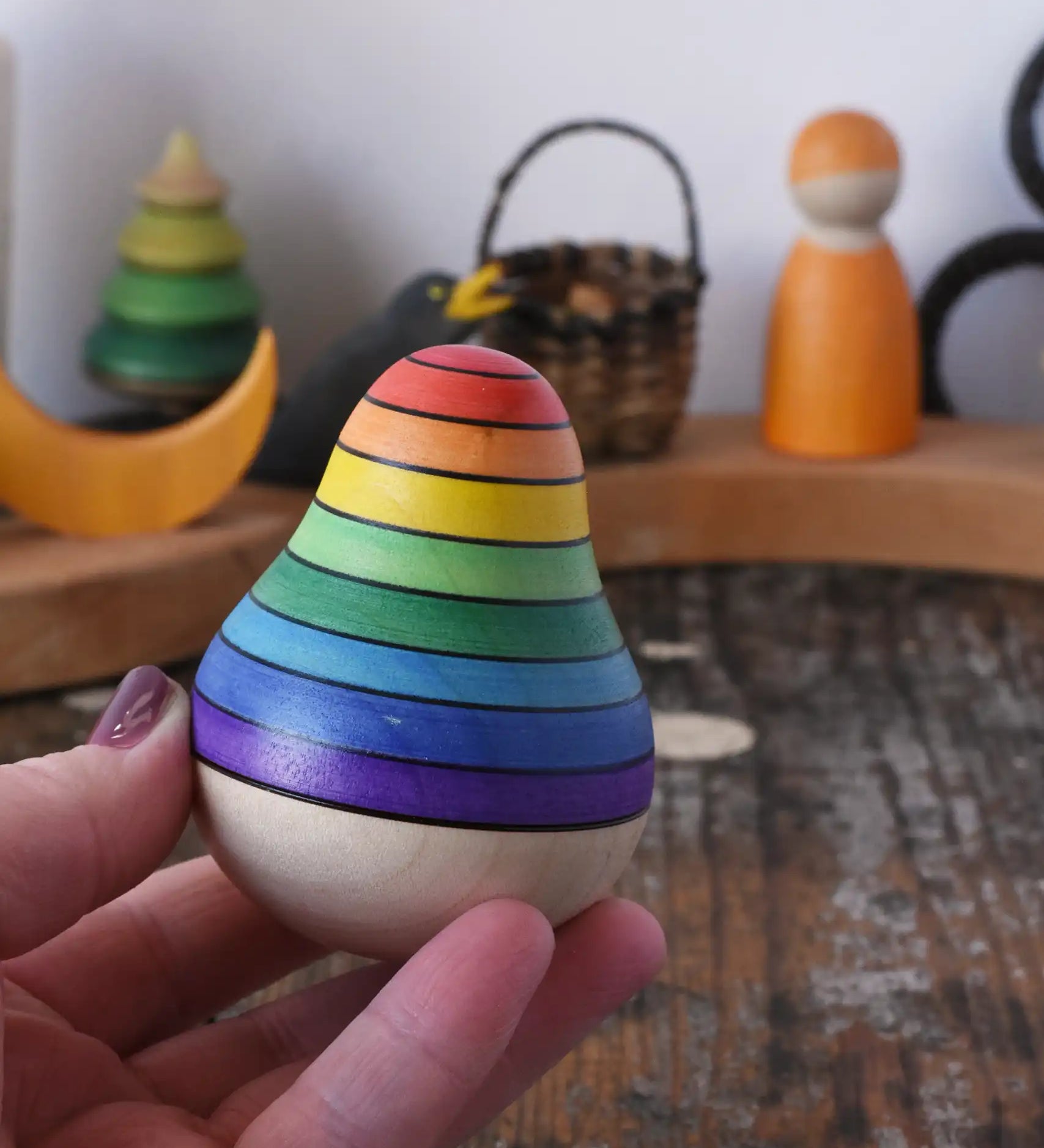 Mader wooden rainbow roly-poly wobbly pear toy in an adult's hand in the Babipur playroom.