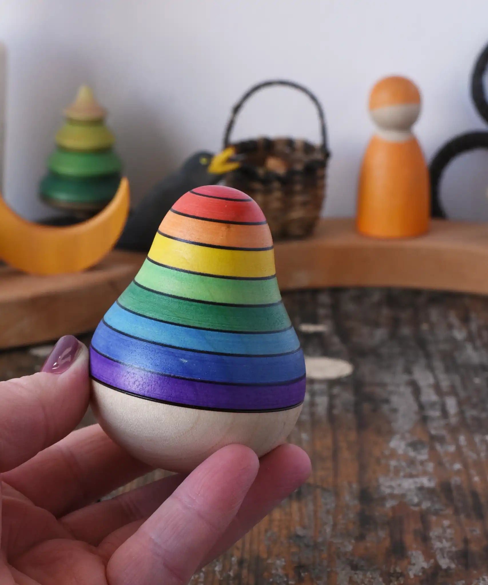 Mader wooden rainbow roly-poly wobbly pear toy in an adult's hand in the Babipur playroom.