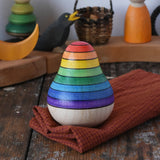 Mader wooden rainbow roly-poly wobbly pear toy placed on a cloth on a wooden surface in the Babipur playroom.